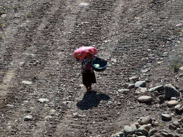 Las personas en Choluteca ya están acostumbradas al calor por las altas temperaturas. En la imagen aparece una mujer cargando un saco sobre la cabeza en una calle de tierra. El sol de la tarde hace que la sombra se refleje en la tierra.