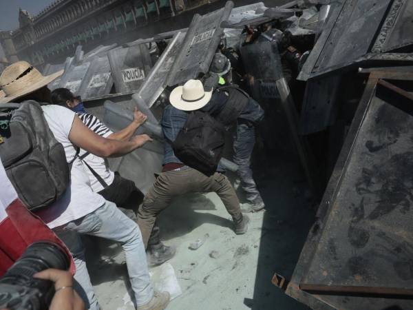 El recorrido inició en el Ángel de la Independencia como una marcha pacífica y terminó en la plaza más grande del país, donde el bloque negro de la manifestación golpeó con martillos y piedras las vallas que resguardaban el Palacio Nacional hasta derribarlas. Aquí las imágenes de los fuertes disturbios.