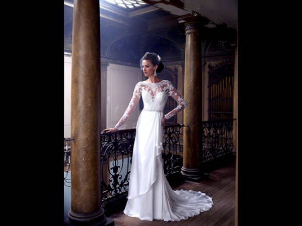 This publicity photo provided by David Tutera for Mon Cheri shows a satin faced chiffon, lace appliqué and tulle wedding dress sheath available in ivory or white. It has illusion and hand-beaded lace long sleeves, illusion and beaded scalloped lace bateau neckline over a plunging sweetheart bodice with re-embroidered lace appliqués and hand-beaded accents, a jewel beaded natural waistband, plunging scalloped V-back neckline, side draped skirt with cascading ruffle and chapel length train. The Berger Collection for Mon Cheri veil is sold separately. (AP Photo/David Tutera for Mon Cheri)