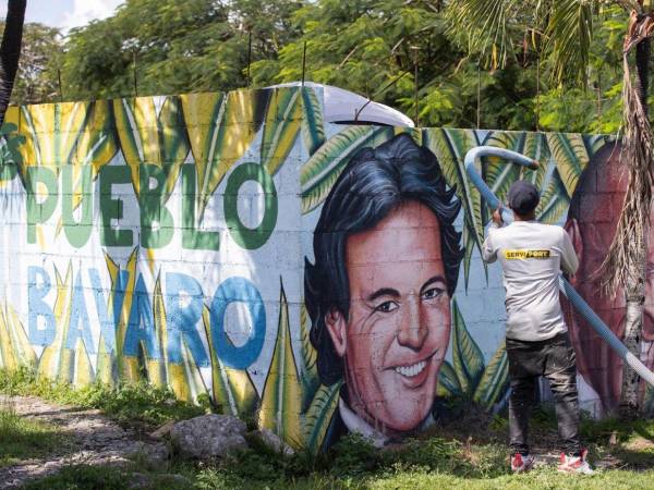 Un ciudadano realiza labores de limpieza frente a un mural con los rostros de los artistas Julio Iglesias y Johnny Ventura en Punta Cana.