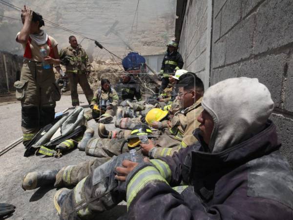 Bajo el sol y con fatiga en sus rostros, elementos del Cuerpo de Bomberos continúan con las labores de rescate para sacar al total del personal que quedó atrapado, luego de que un cerro se desplomara y provocara un incendio que causó pérdidas materiales en una bodega en el anillo periférico.