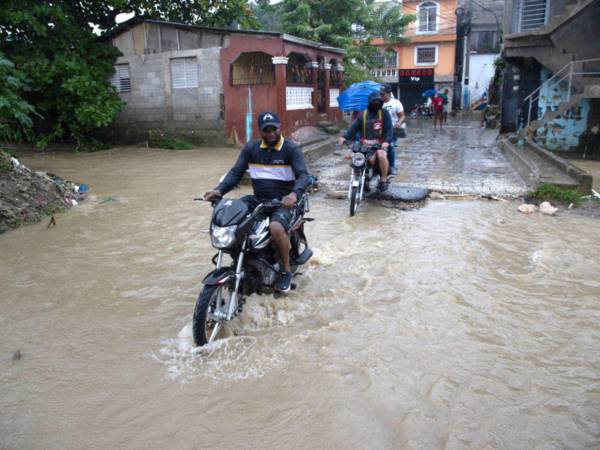Personas cruzan una cañada desbordada en el barrio Manoguayabo este viernes, en Santo Domingo (República Dominicana). La tormenta tropical Melissa, que mantiene un comportamiento errático y casi estacionario, ha causado un muerto y fuertes inundaciones en la República Dominicana.