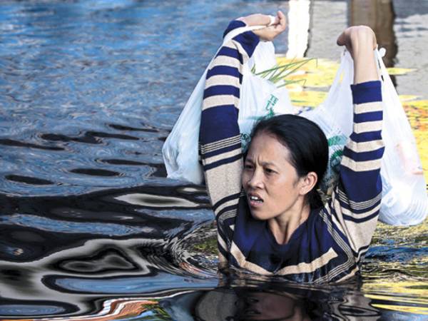 A woman carries bags of food and supplies above her shoulder while walking in the chest-high flood water in Ban Bang Bua Thong district in central Thailand's Nonthaburi province.