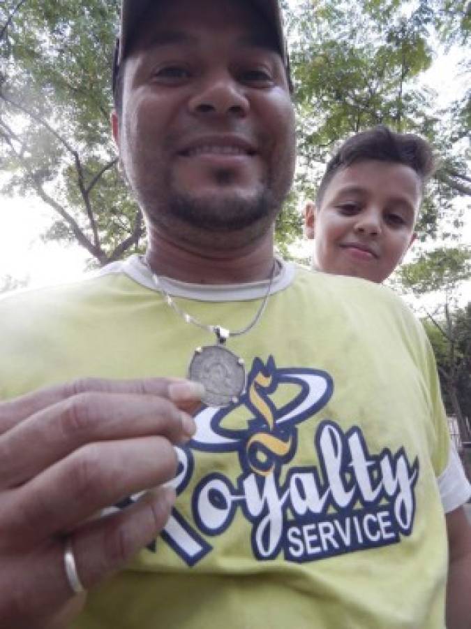 Este hombre muestra una moneda hondureña que lleva sobre su pecho durante su vida en España. Su hijo lo observa.
