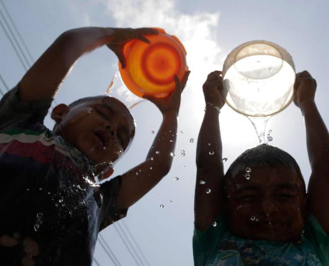 Niños hondureños mitigan el calor bañándose con un poco de agua en el departamento de Cortés.