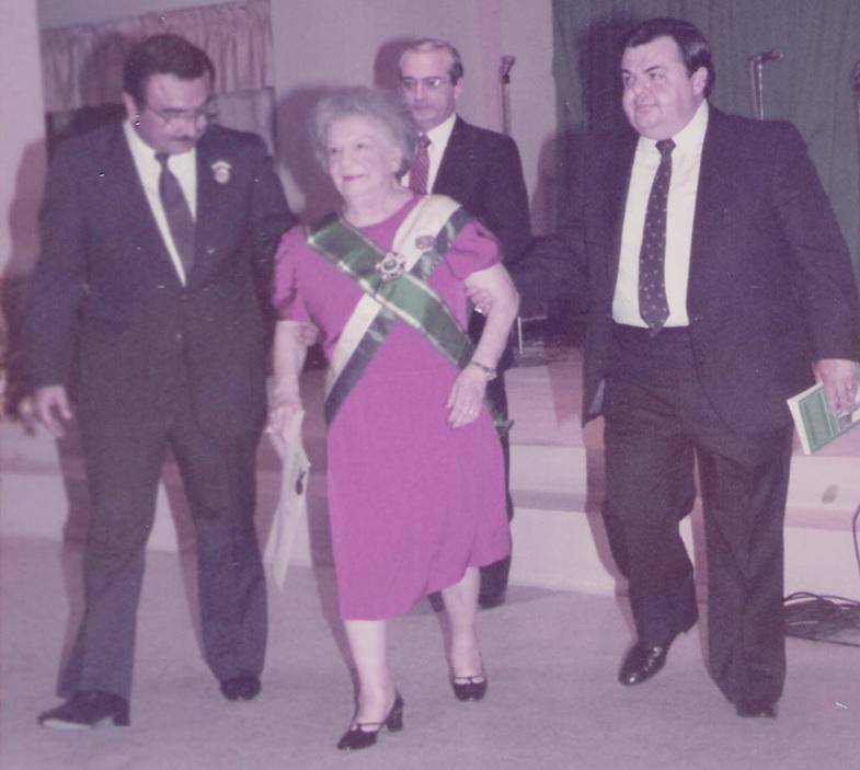 Don Nahúm Valladares camina por la izquierda, sosteniendo a doña Rosario Sagastume de Ferrari, mientras don José Rafael Ferrari lo acompaña por la derecha, junto a Manuel Villeda, en un momento de homenaje y reconocimiento.