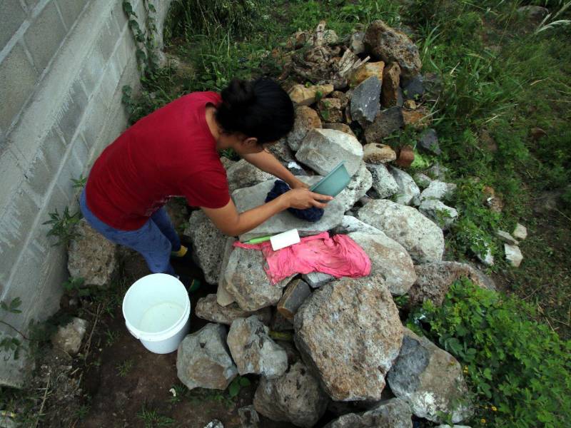 Liliana Aguiluz dosifica con un pequeño recipiente el agua de un balde para lavar ropa sobre una pila improvisada de piedras en la colonia El Amatillo, Comayagüela.