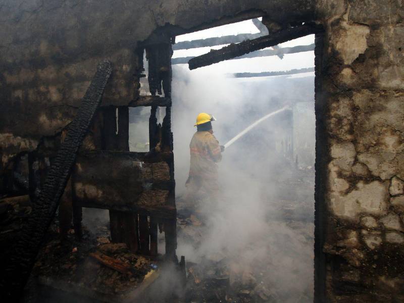 Un bombero realiza labores de extinción del incendio en las paredes de bahareque de la vivienda.