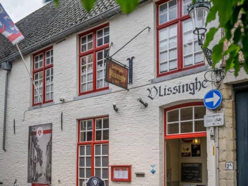 La fachada de Café Vlissinghe exhibe una bandera del pueblo de Brujas, un rótulo antiguo con su nombre y un menú que destaca sus meriendas estrellas.