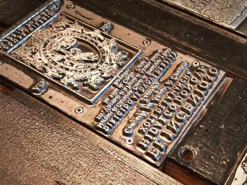 La fotografía a detalle de una de las planchas metálicas permite apreciar con nitidez los grabados en relieve y las letras invertidas que componían los textos originales.