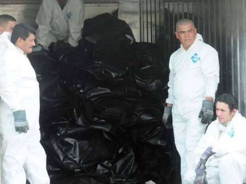 La imagen recoge una de las escenas dramáticas del 14 de febrero de 2012, el personal forense toma un breve respiro junto a una pila de cuerpos carbonizados que yacen en bolsas de morgue tras el peor incendio registrado en una cárcel hondureña. Este sábado se cumplen 14 años de esa tragedia.