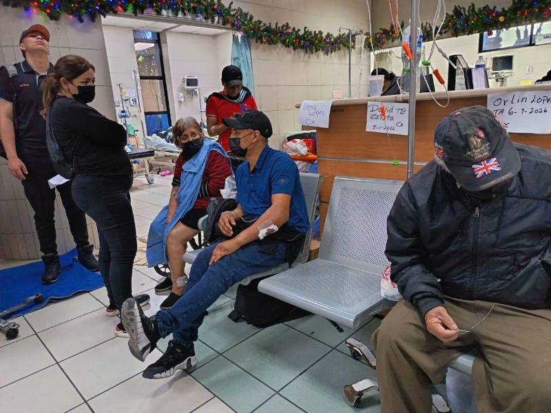 Los pacientes internos esperan una camilla sentados en una silla identificados con sus nombres.