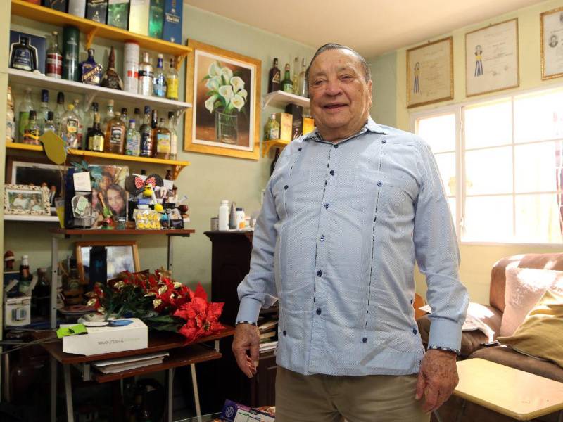 El doctor Augusto Aguilar posando junto a su guaroteca, un espacio donde guarda todas las bebidas que le han regalado en los lugares en los que ha participado como observador electoral.