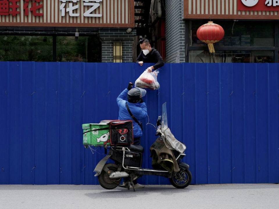 En esta foto de archivo tomada el 11 de mayo de 2022, un repartidor pasa artículos a un hombre dentro de un área residencial cercada bajo un bloqueo de coronavirus Covid-19 en Beijing.
