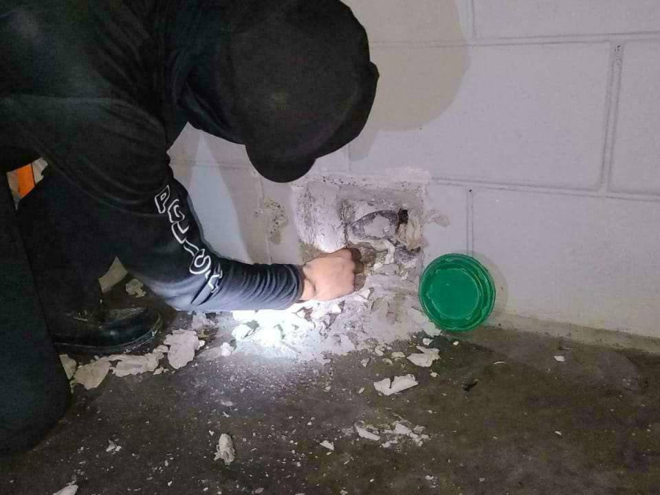 Un agente penitenciario escarba en una de las caletas donde los miembros de la Pandilla 18 guardaban sus armas.