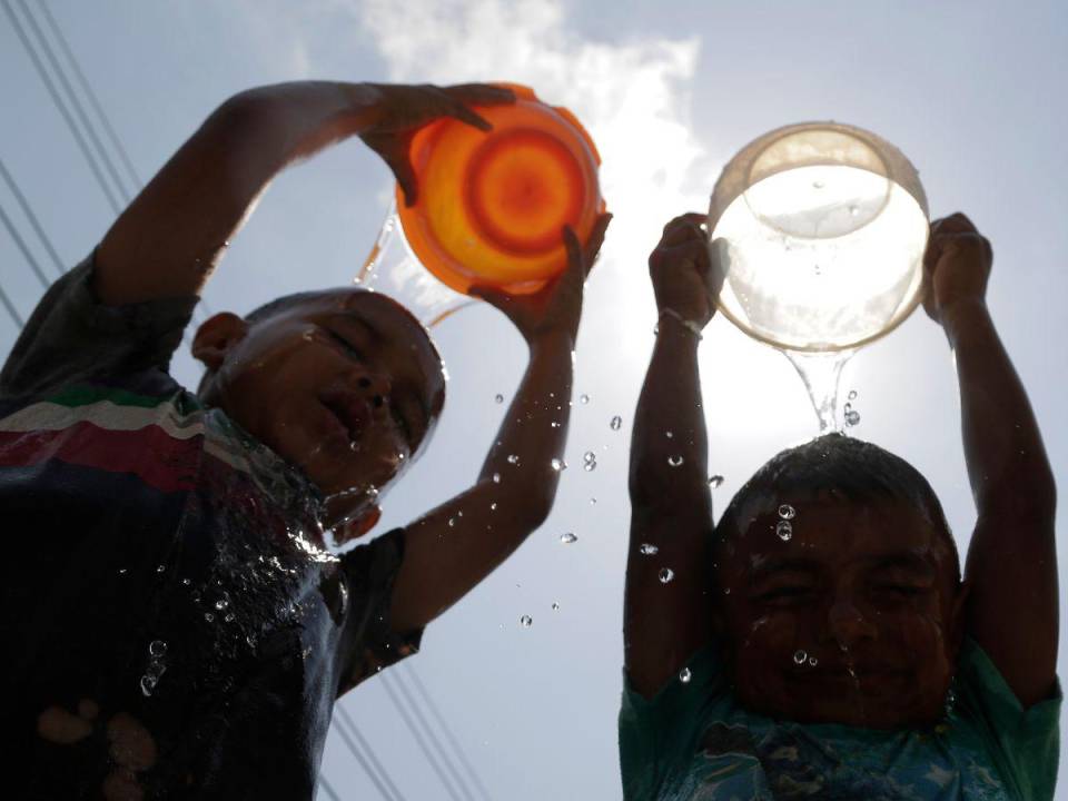 Niños hondureños mitigan el calor bañándose con un poco de agua en el departamento de Cortés.