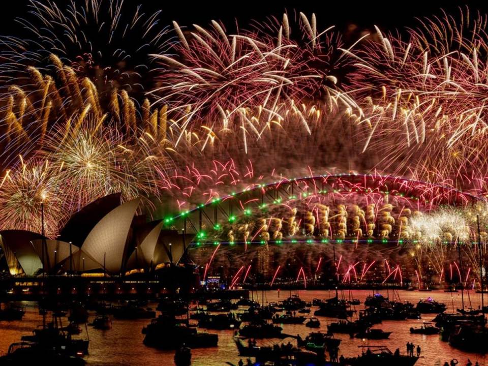 Los fuegos artificiales explotan sobre el puente del puerto de Sídney y la Ópera de Sídney (izq.) durante las celebraciones de Nochevieja en Sídney el 1 de enero de 2024.