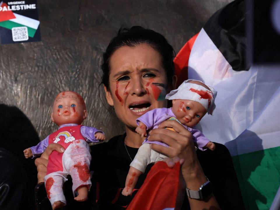 Una mujer sostiene dos muñecos pintados como si estuvieran lastimados, representando a los bebés en Palestina tras los bombardeos de Israel.