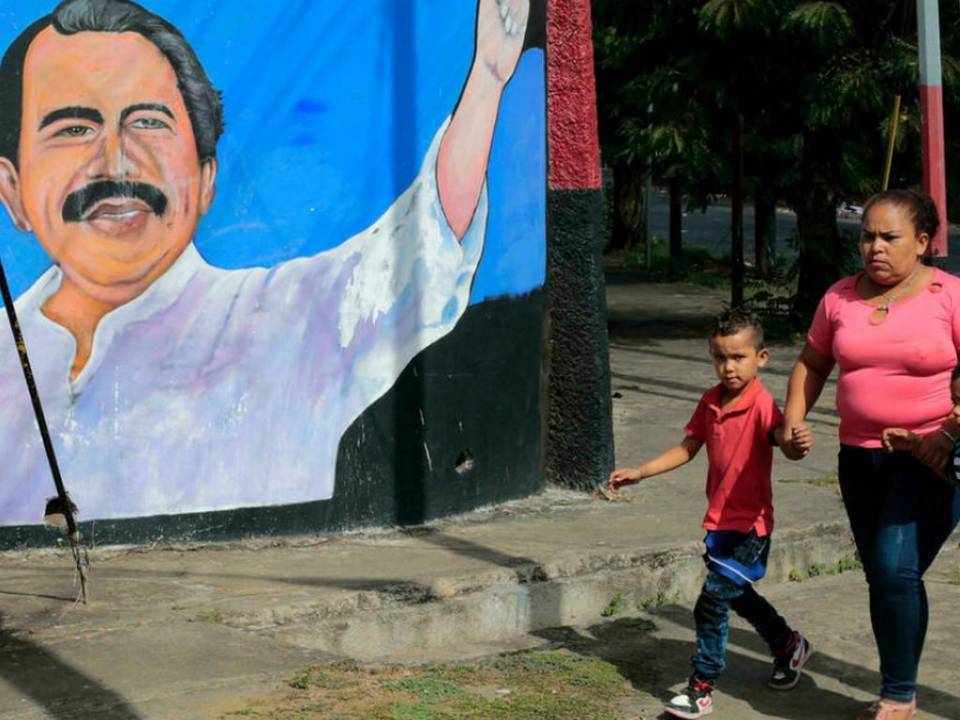 Una mujer y niños caminan junto a un mural que representa al presidente de Nicaragua, Daniel Ortega, en Managua el 10 de enero de 2022, día en que inicia su cuarto mandato.