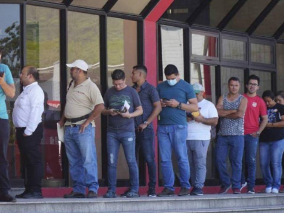 Imagen de archivo que muestra a varias personas haciendo fila frente a una agencia bancaria.