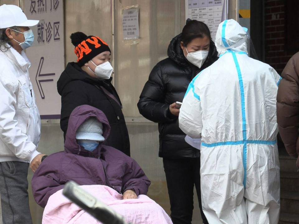 Esta captura de fotograma de un video de AFPTV muestra a una mujer hablando con un trabajador de la salud mientras la gente hace cola afuera de una clínica de fiebre en medio de la pandemia de covid-19 en Beijing el 14 de diciembre de 2022.