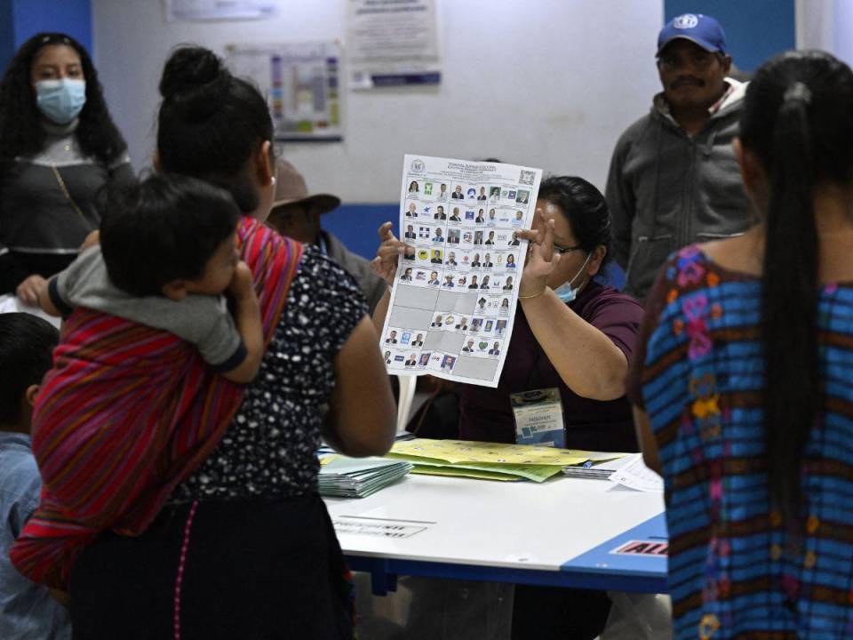 Una votante que lleva a un niño a la espalda recibe instrucciones de un encargado de un colegio electoral en San Juan Sacatepéquez, 40 km al oeste de la ciudad de Guatemala, el 25 de junio de 2023.