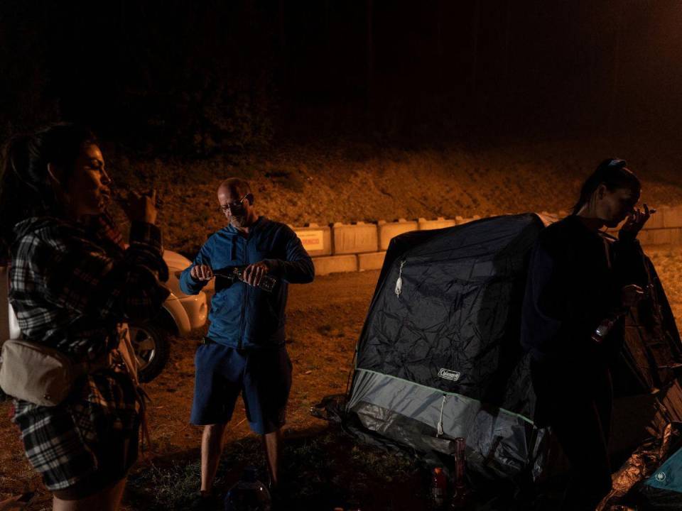 Los miembros de la familia Shay Nicole, Eren Loney y Shannon Fiddler se cepillan los dientes en un estacionamiento en el Jim Lind Arena después de registrarse en los Servicios de Apoyo de Emergencia después de recibir la orden de abandonar el lago Shannon mientras continúan los incendios forestales de McDougall Creek en West Kelowna, Columbia Británica, el 19 de agosto. , 2023.