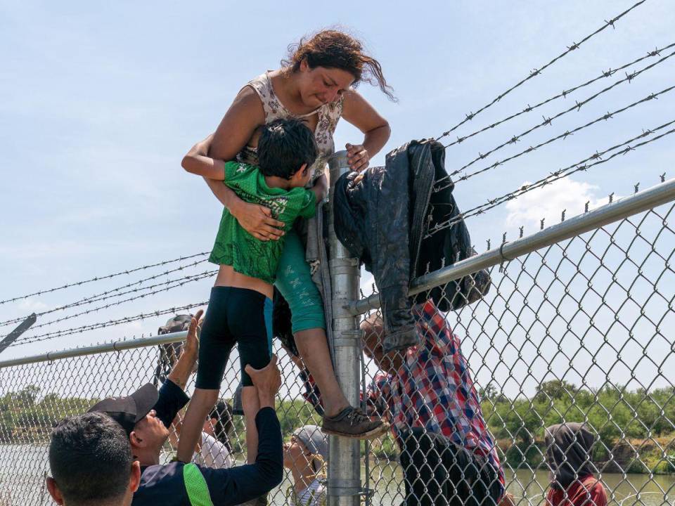 Una madre ayuda a su hijo a pasar la valla de alambre de púas en Eagle Pass, Texas, después de cruzar a Estados Unidos desde México el 25 de agosto de 2023.